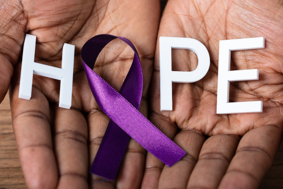 Two hands holding letters spelling the word HOPE where the "O" is formed by a purple ribbon.